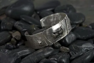 Silver bracelet with a black stone on river rock background.
