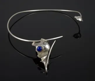 Silver necklace with blue stone on black surface.