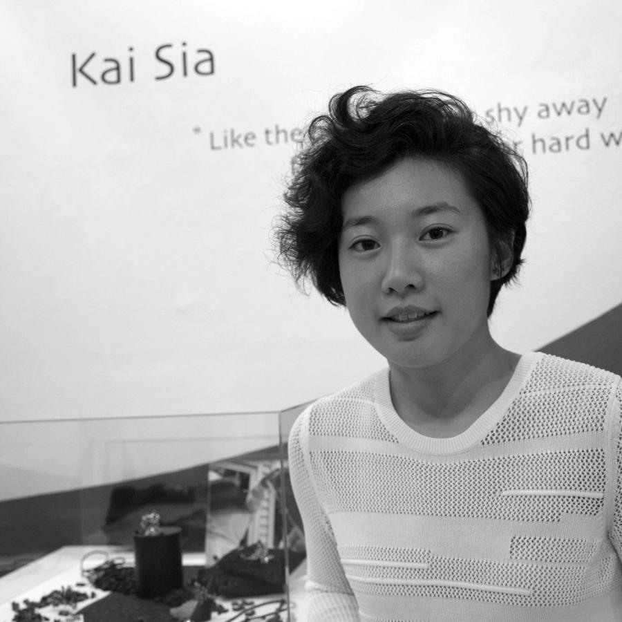 Kai standing by her work and name display