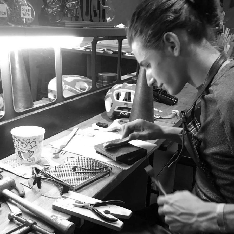 A young artisan focuses on crafting jewelry at a cluttered workbench.