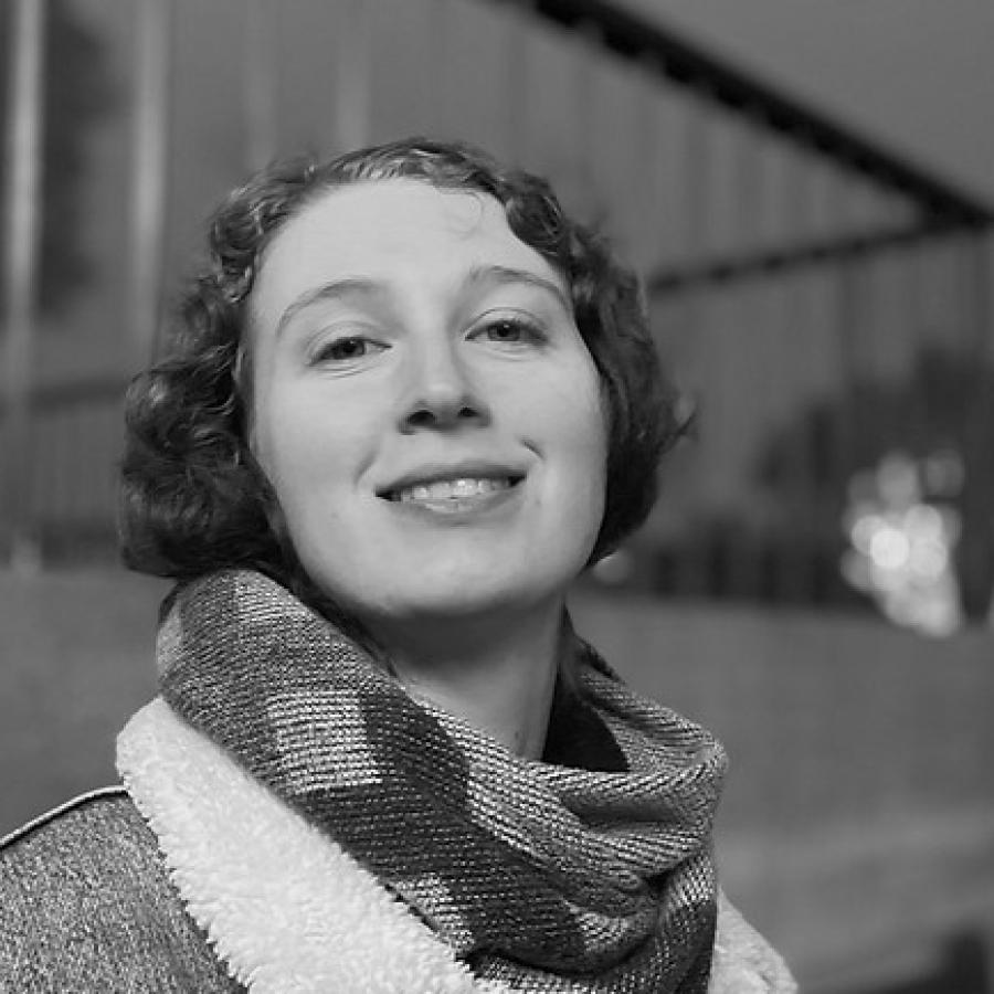 A photograph of a young person smiling outdoors at dusk, wearing a denim jacket and scarf.