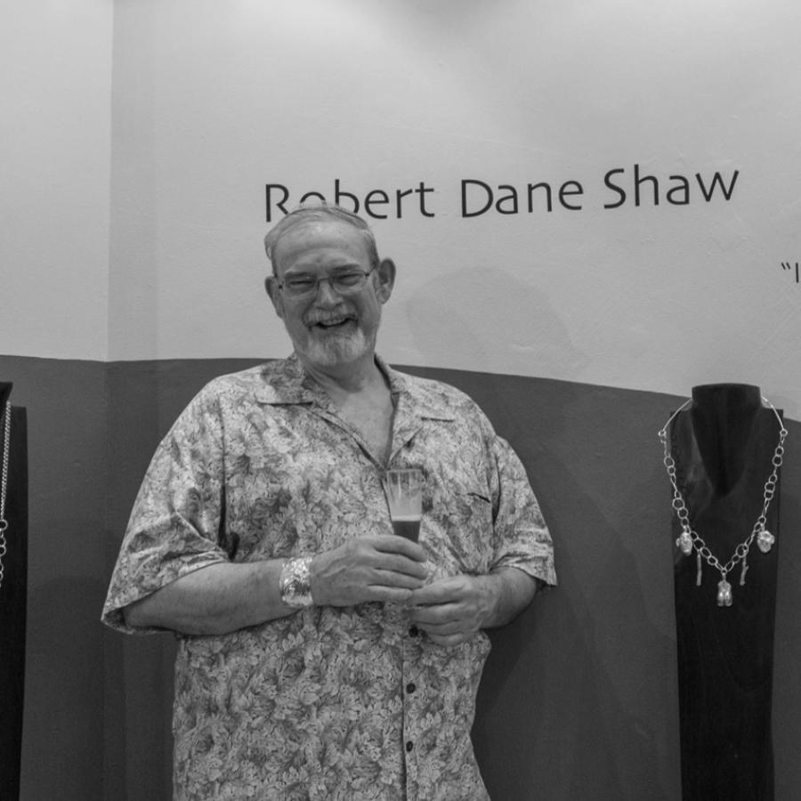 Photograph of a smiling man in a yellow shirt standing next to jewelry displays.