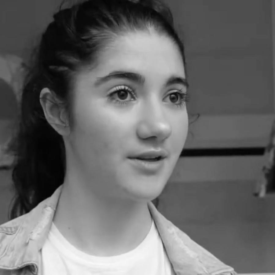 Close-up photograph of a young woman with brown hair, a denim jacket, and a graphic t-shirt.