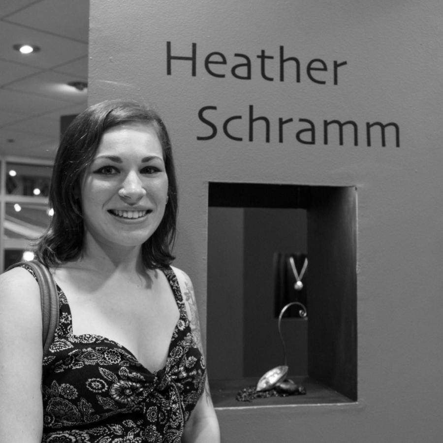 Photograph of a woman smiling, standing beside an orange pillar with the name Heather Schramm.