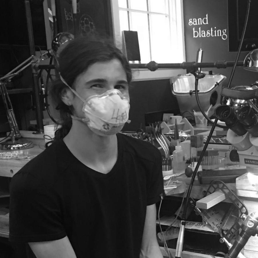 A young person wearing a mask sits in a well-equipped workshop.