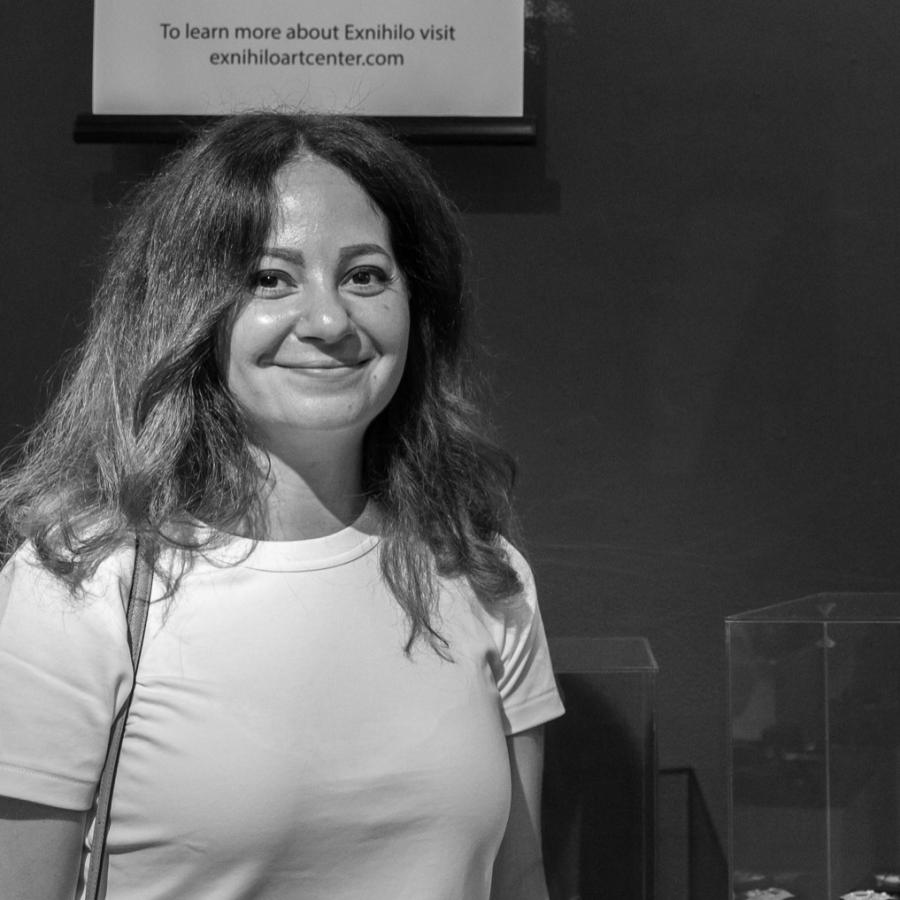 Photograph of a woman smiling in front of an art exhibition wall.