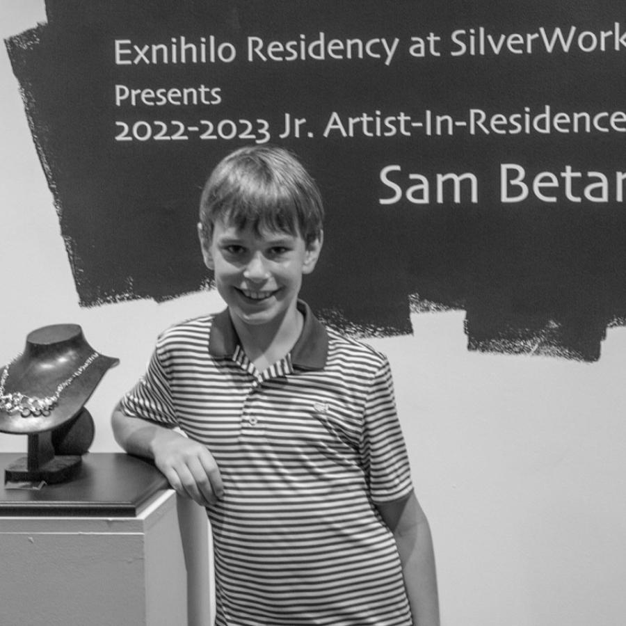 Photograph of a woman and boy smiling next to a pedestal with artwork.