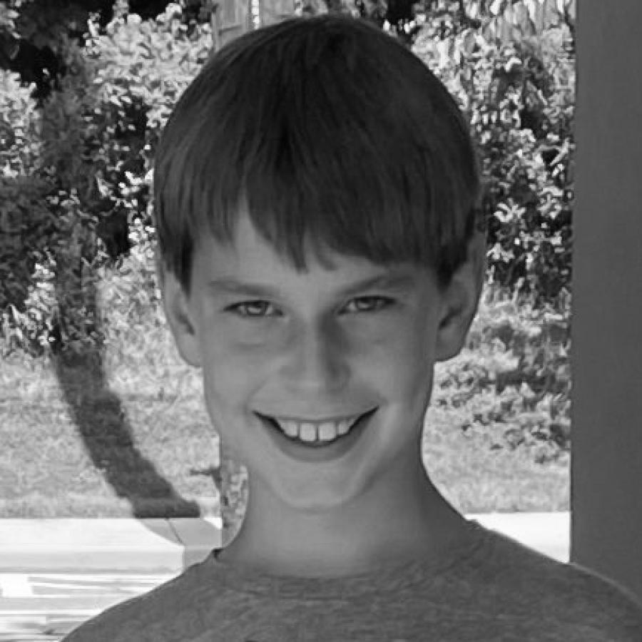 Photograph of a boy smiling in a grey shirt outdoors.