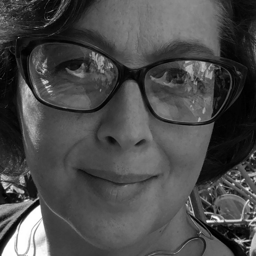 Black and white photograph of a woman wearing glasses smiling outdoors.