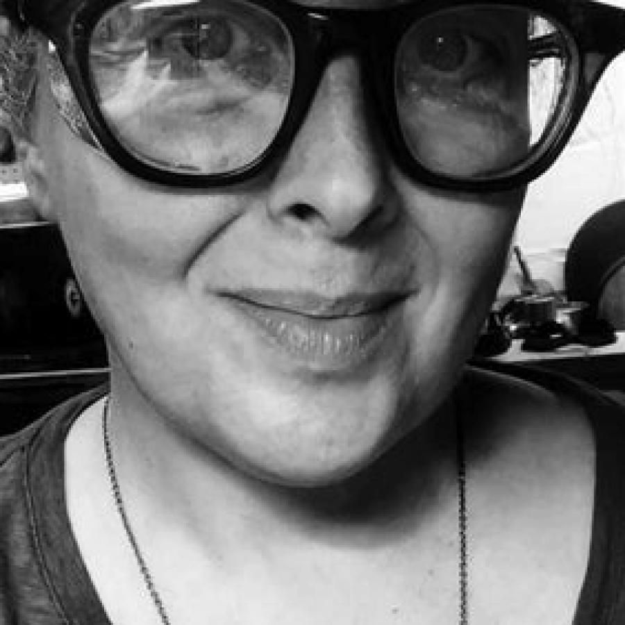 Black and white portrait of a smiling woman in thick glasses and a wave necklace.