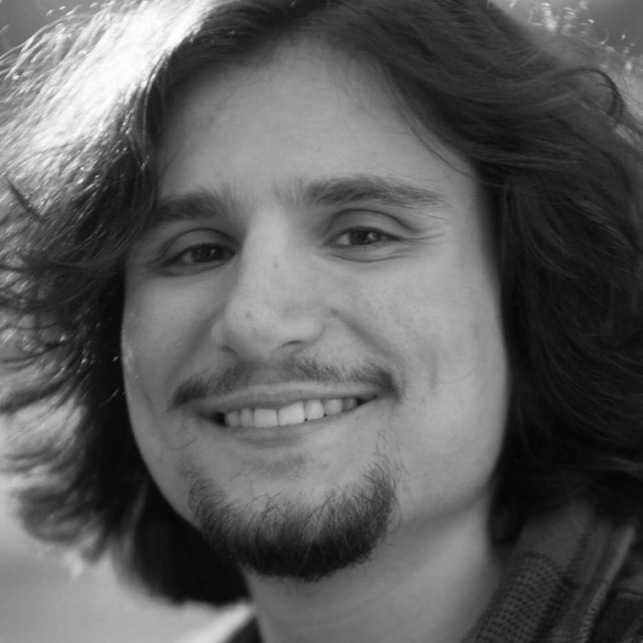 Black and white close-up photograph of a smiling young man with long dark hair and a goatee.