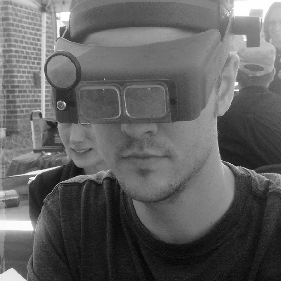 A sepia-toned photograph of a man wearing magnifying visor glasses working on a small metal object.