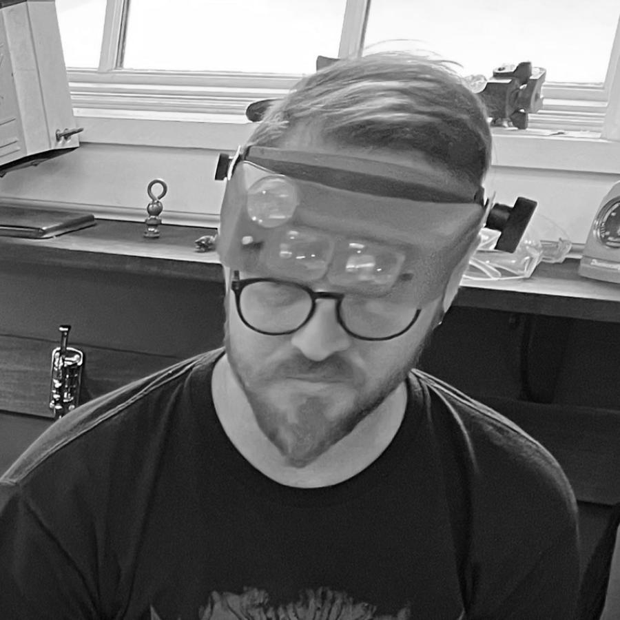 Photo of a man wearing magnifying headgear sitting next to a smiling woman in a workshop.
