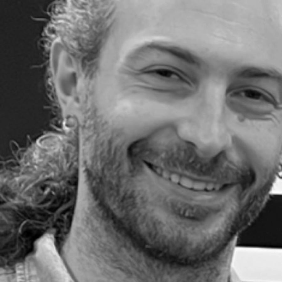 Black and white photograph of a smiling man with a beard and earring.