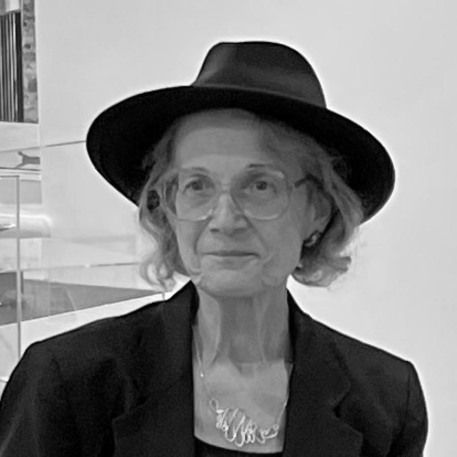 Photograph of a woman in a black fedora and blazer standing in a gallery.