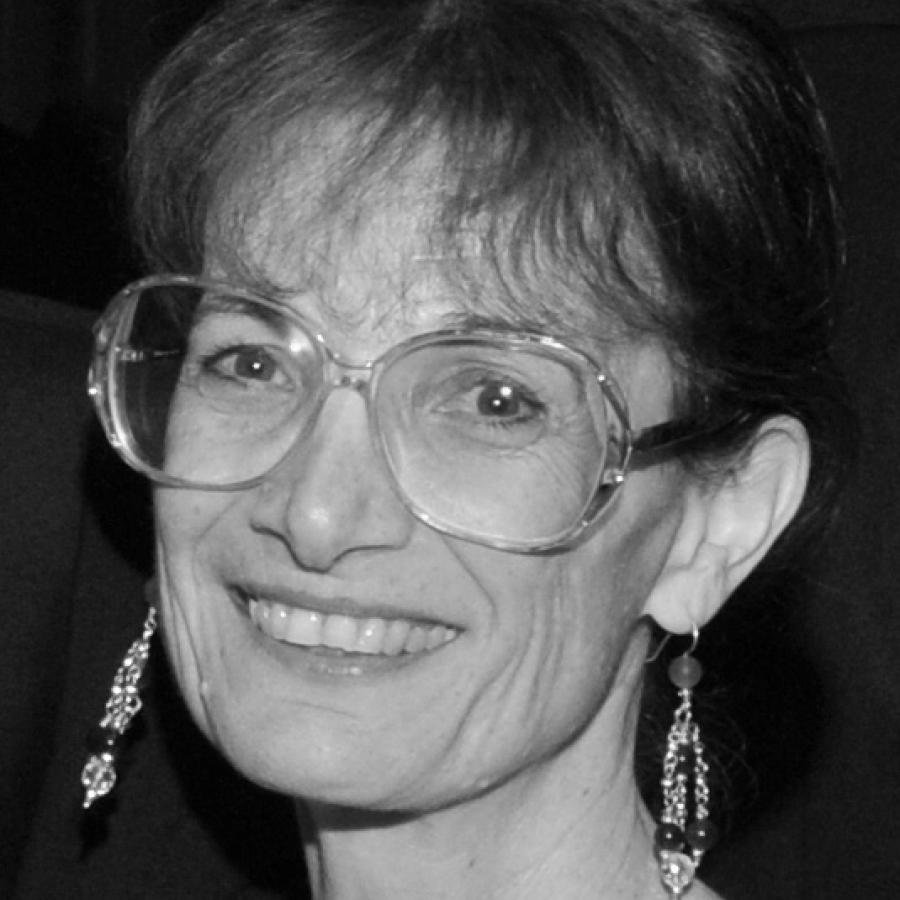 Photograph of a smiling woman wearing large glasses and dangling earrings.