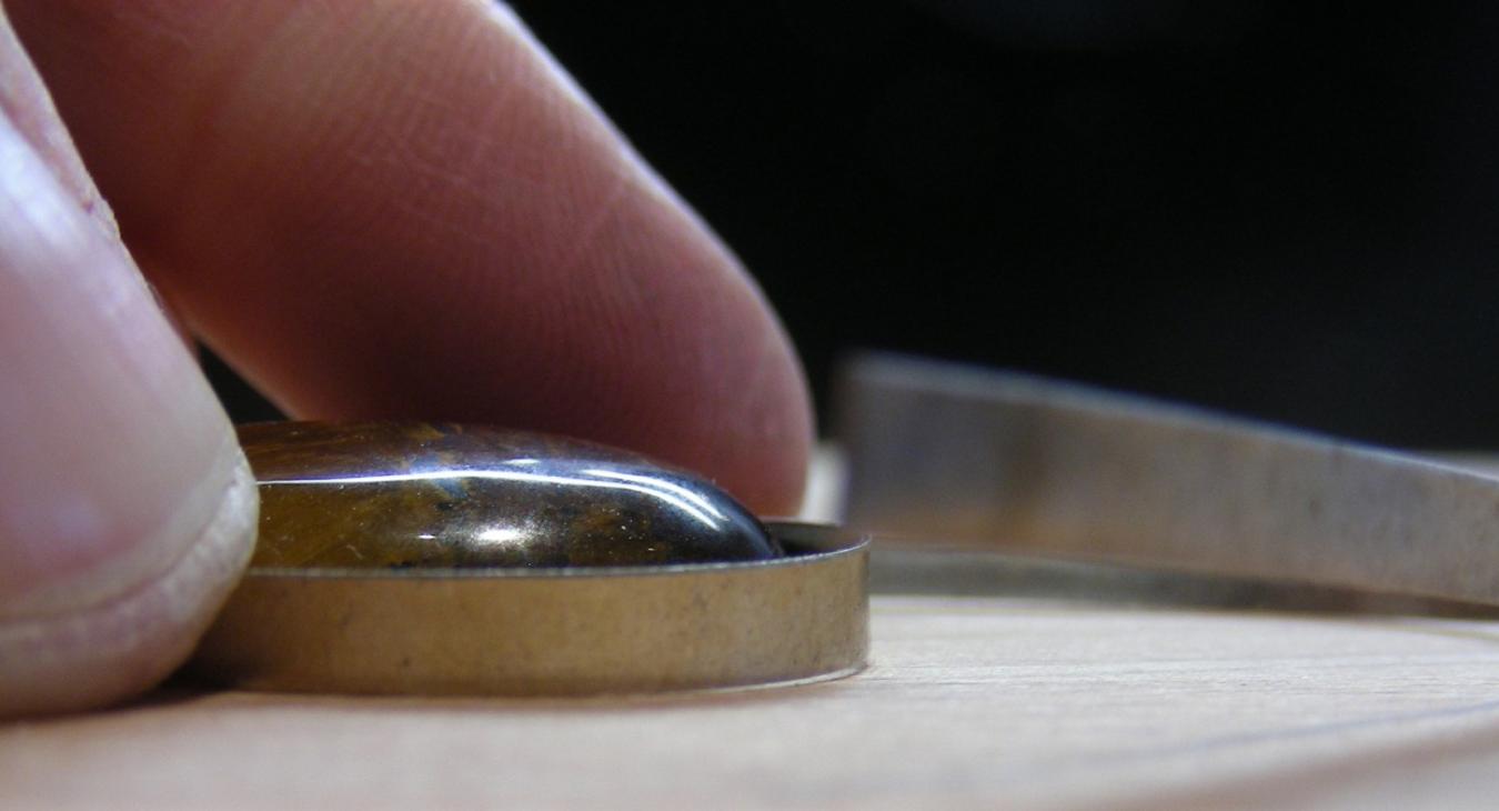 Fingers pushing a cabochon stone into a silver bezel