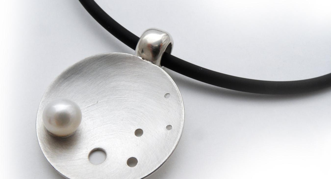 pearl on domed circular silver piece with black neck cord 