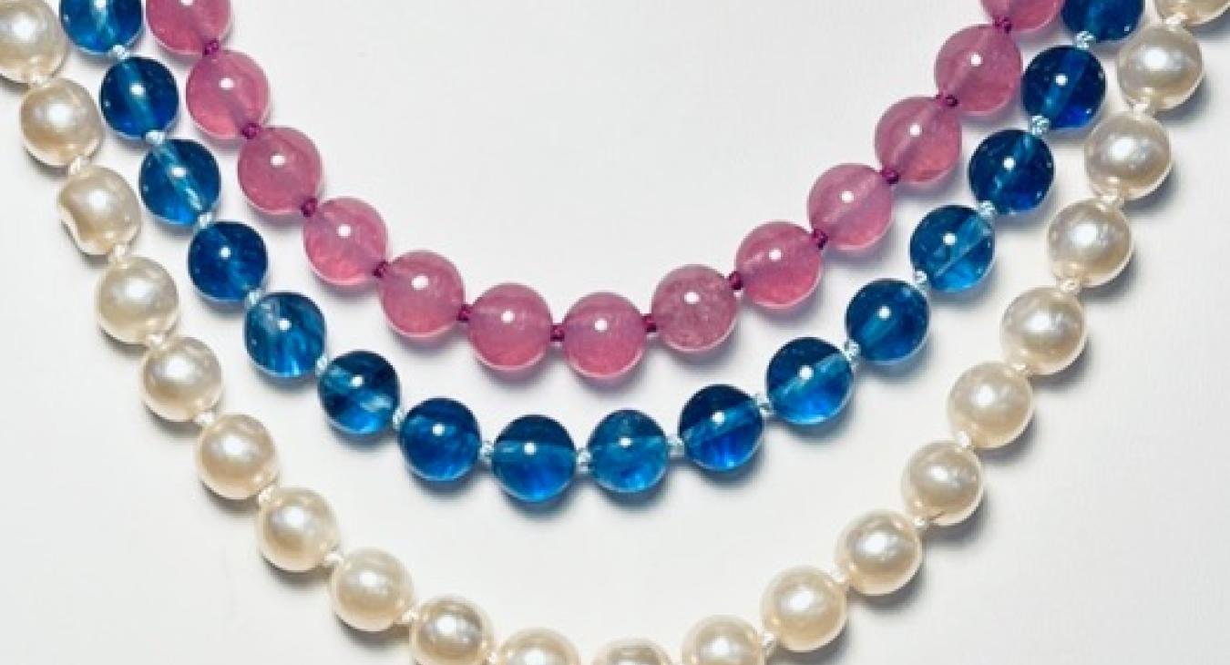 Three beaded necklaces in white, blue, and pink arranged in concentric arcs.