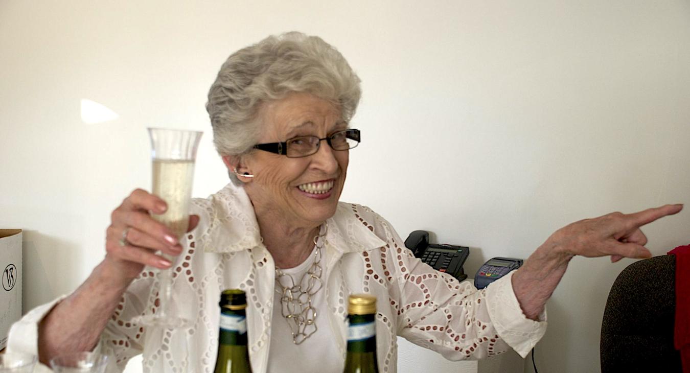 Blair's mother holding champagne and smiling and pointing