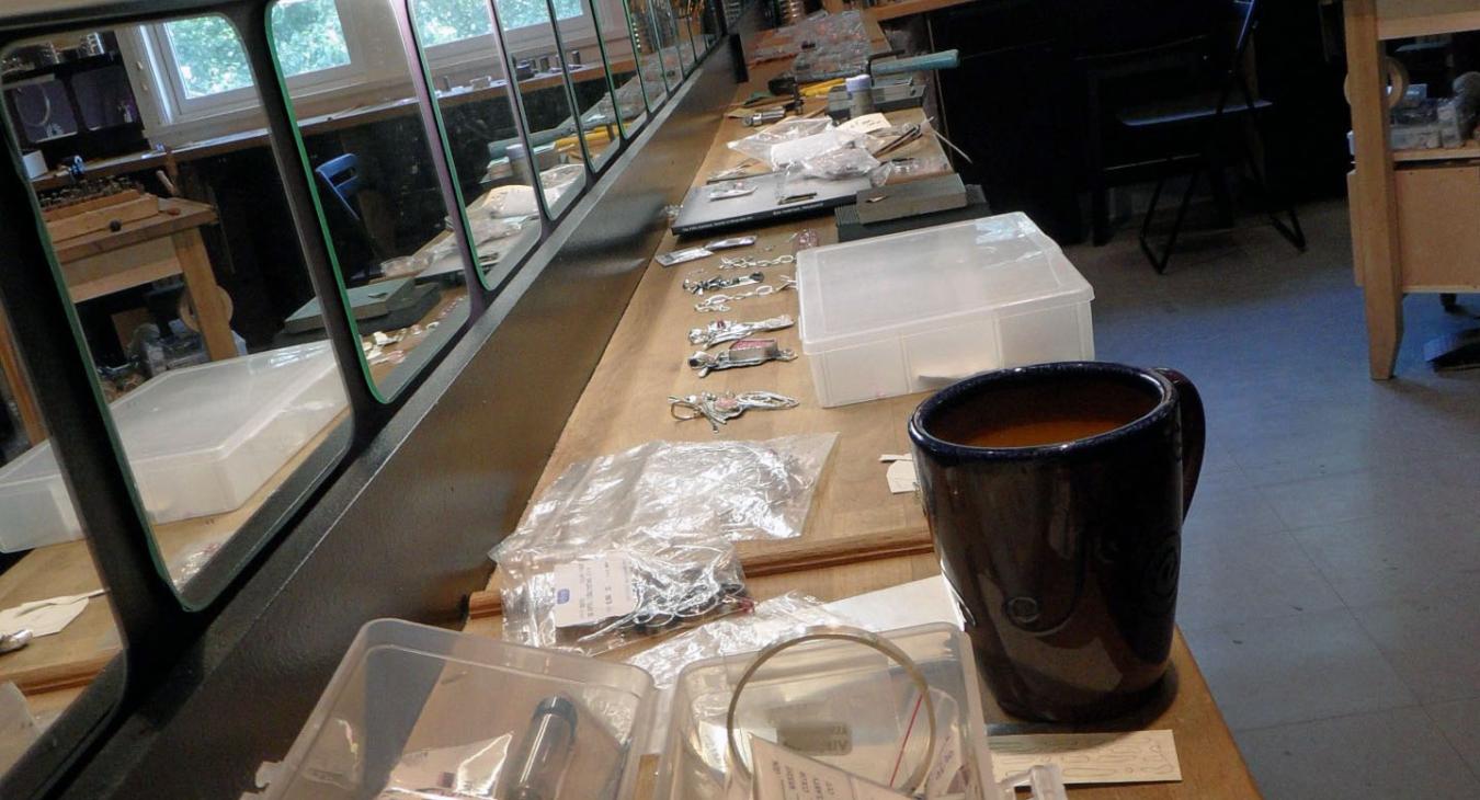 studio one bench covered in tools and works in process, with coffee cup