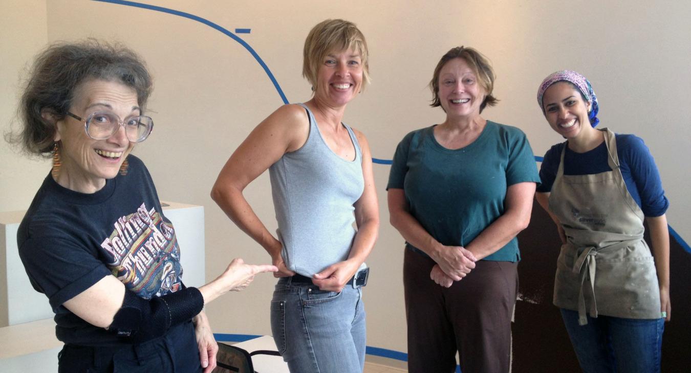 Ruth, Helena, Chantel, & Mawadda posing, ready to paint. Ruth pointing out the tiny speck of paint on Helena’s shirt.