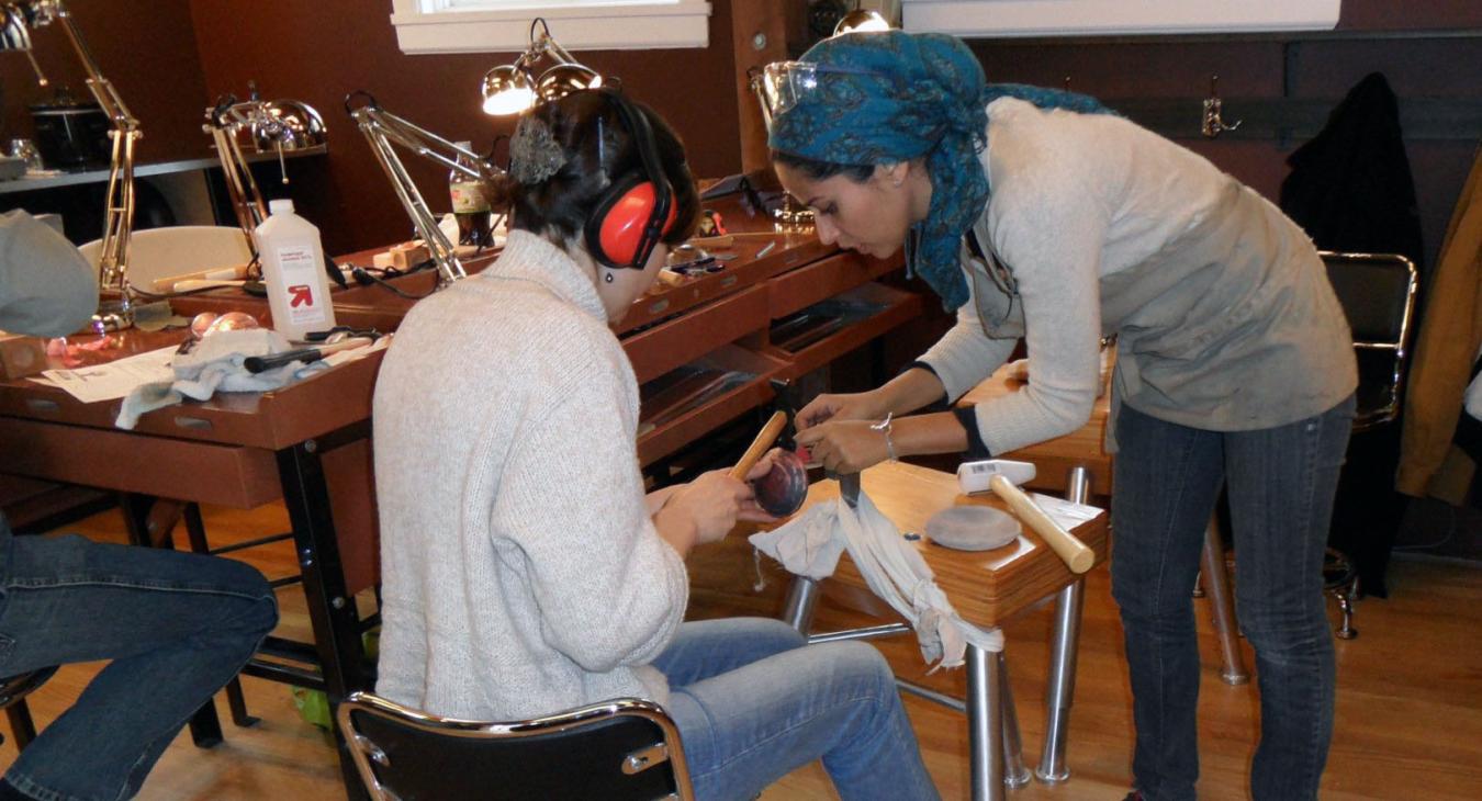 Mawadda leaning over instructing a sitting student on tool use