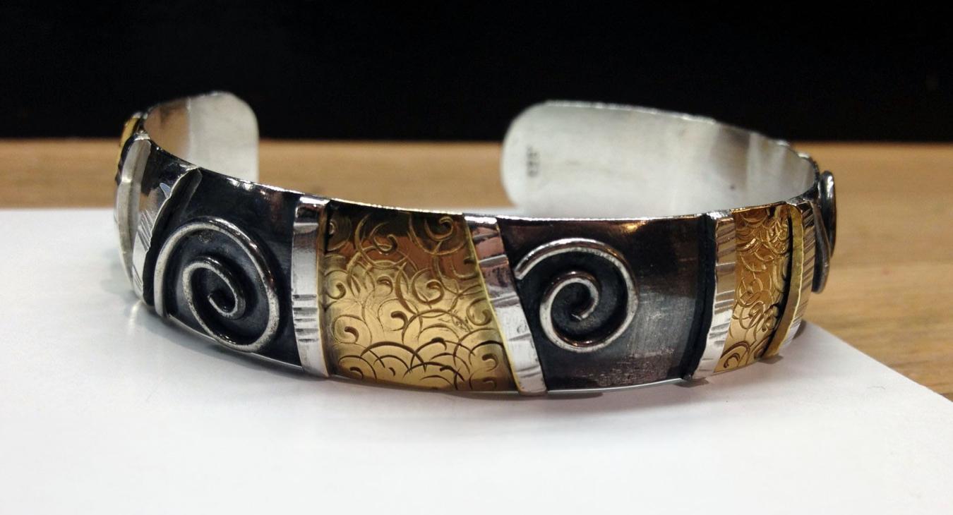 a silver cuff bracelet accented with 24k gold and oxidation