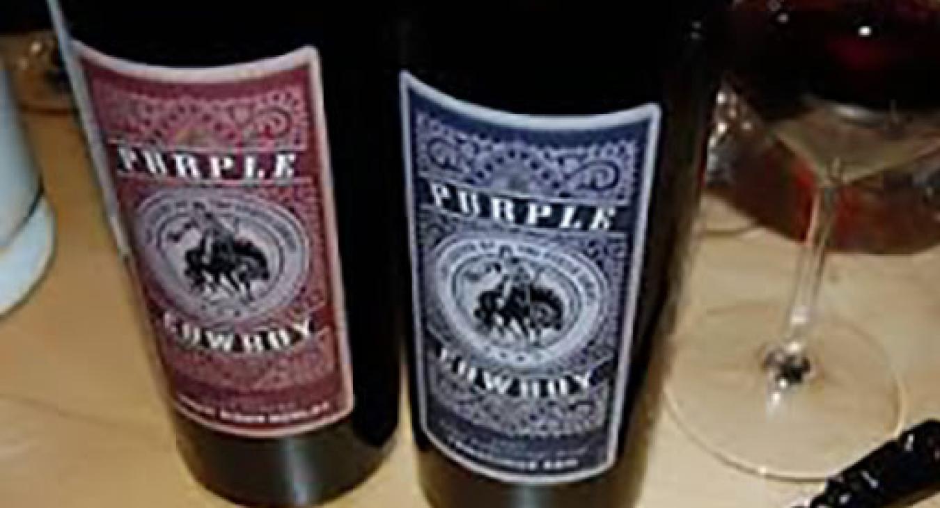 Two bottles of Purple Cowboy wine next to glass and wine opener