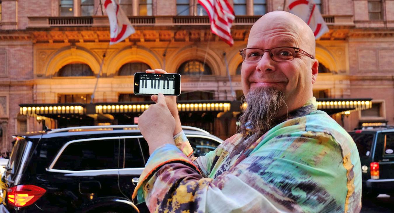 Bryan holding phone with piano keys image in front of Carnegie Hall