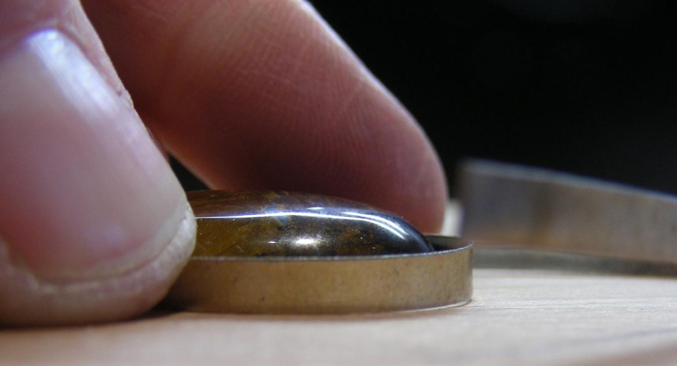 Fingers pushing a cabochon stone into a silver bezel