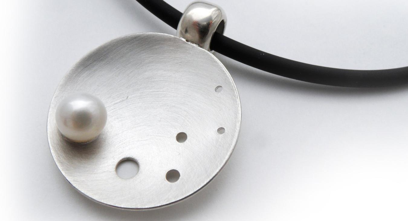 pearl on domed circular silver piece with black neck cord 