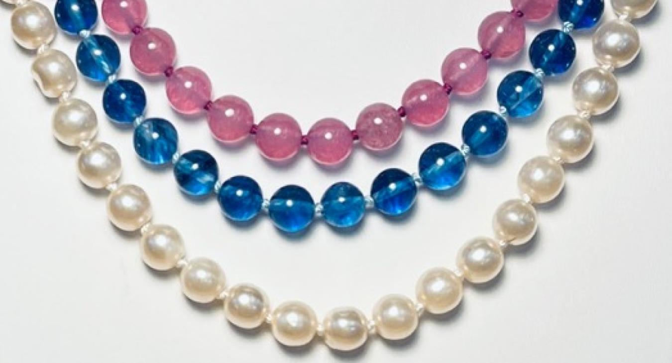 Three beaded necklaces in white, blue, and pink arranged in concentric arcs.