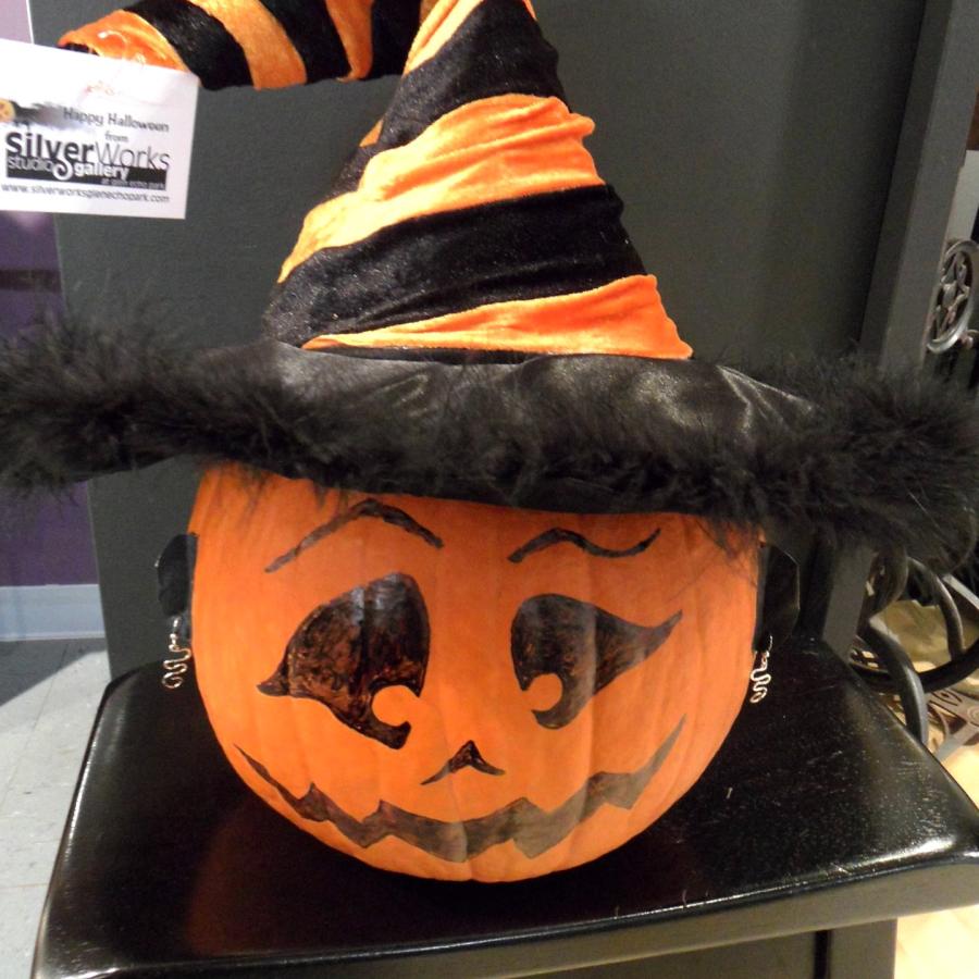 Pumpkin with painted face and black and orange striped witch hat and silver earrings