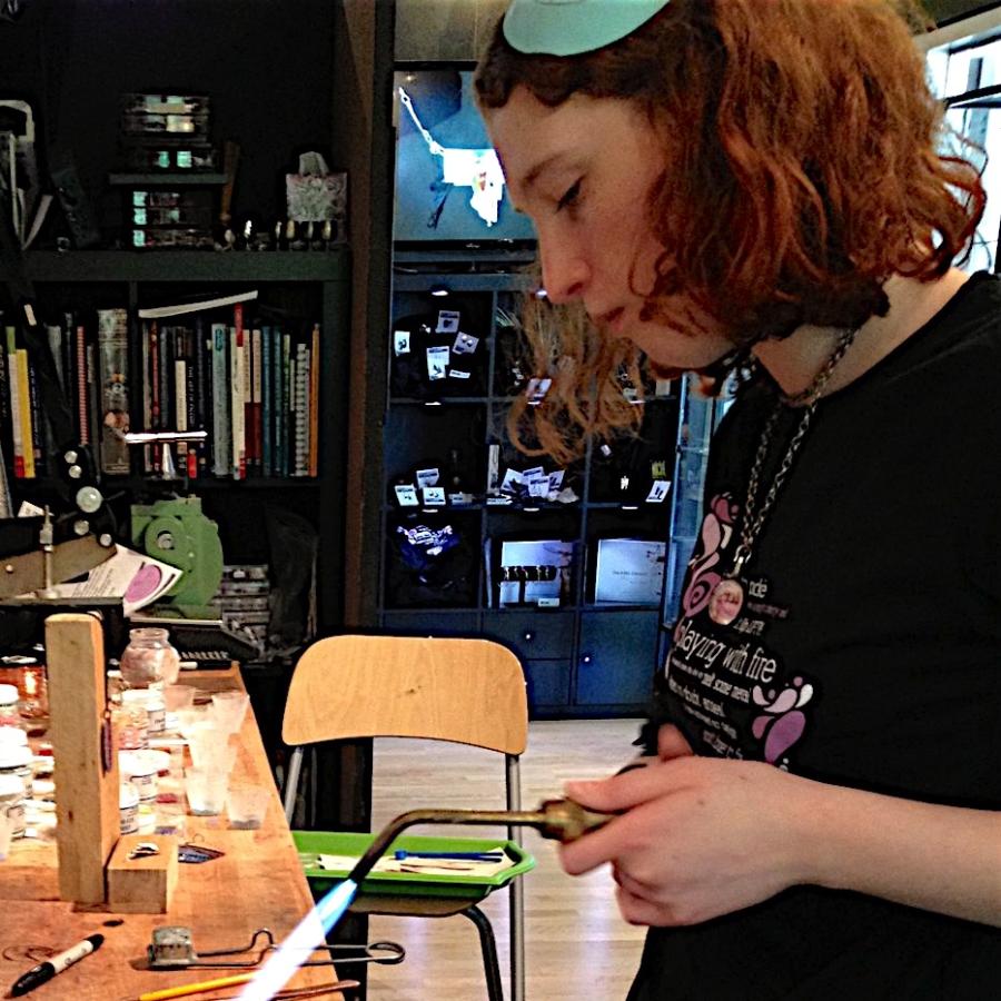 A jeweler works with a soldering torch at a wooden workbench.