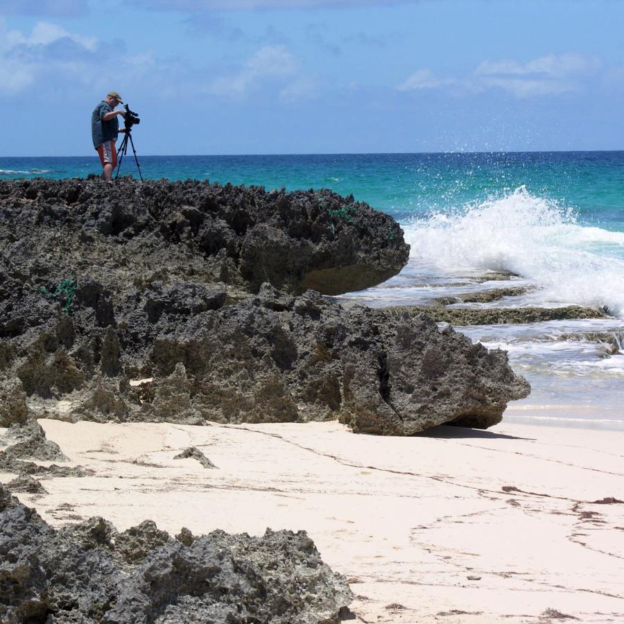 Bryan filming on rocks by the beach