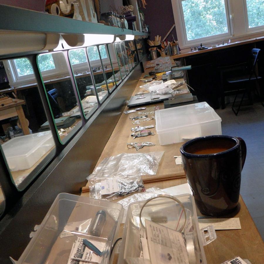 studio one bench covered in tools and works in process, with coffee cup