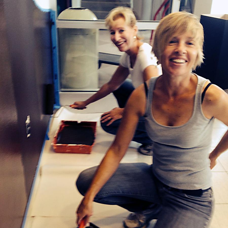 Helena and Joan crouching painting the title wall black 