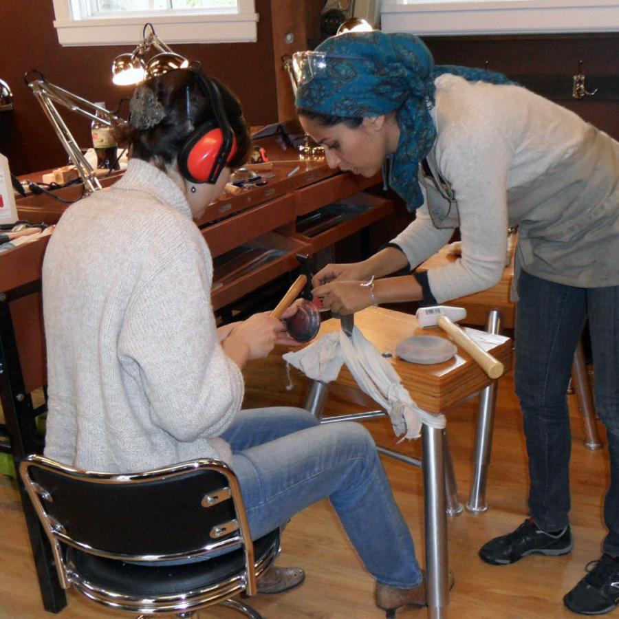 Mawadda leaning over instructing a sitting student on tool use