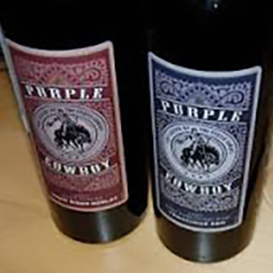 Two bottles of Purple Cowboy wine next to glass and wine opener