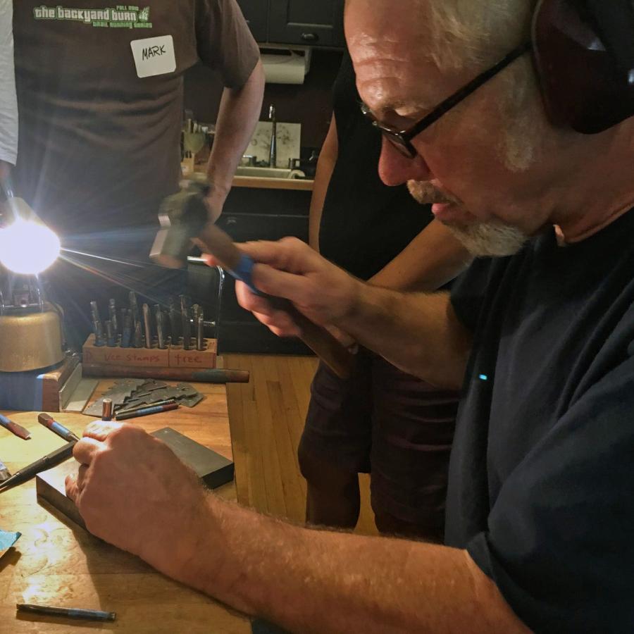 Alan demonstrating hammering a stamp on anvil with students looking on