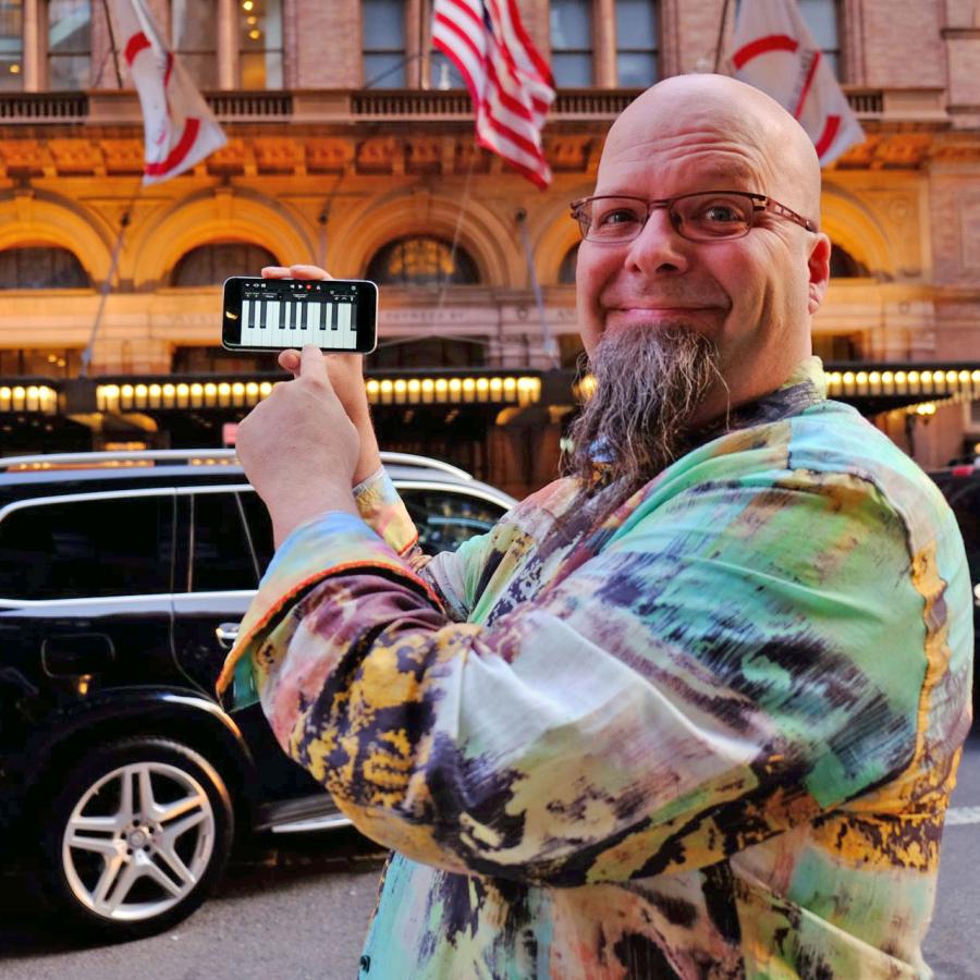 Bryan holding phone with piano keys image in front of Carnegie Hall