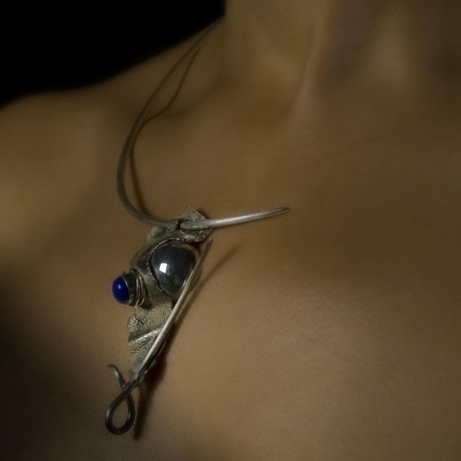 Woman wearing silver necklace against dark background.
