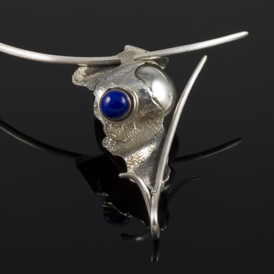 Silver necklace with blue stone on black surface.