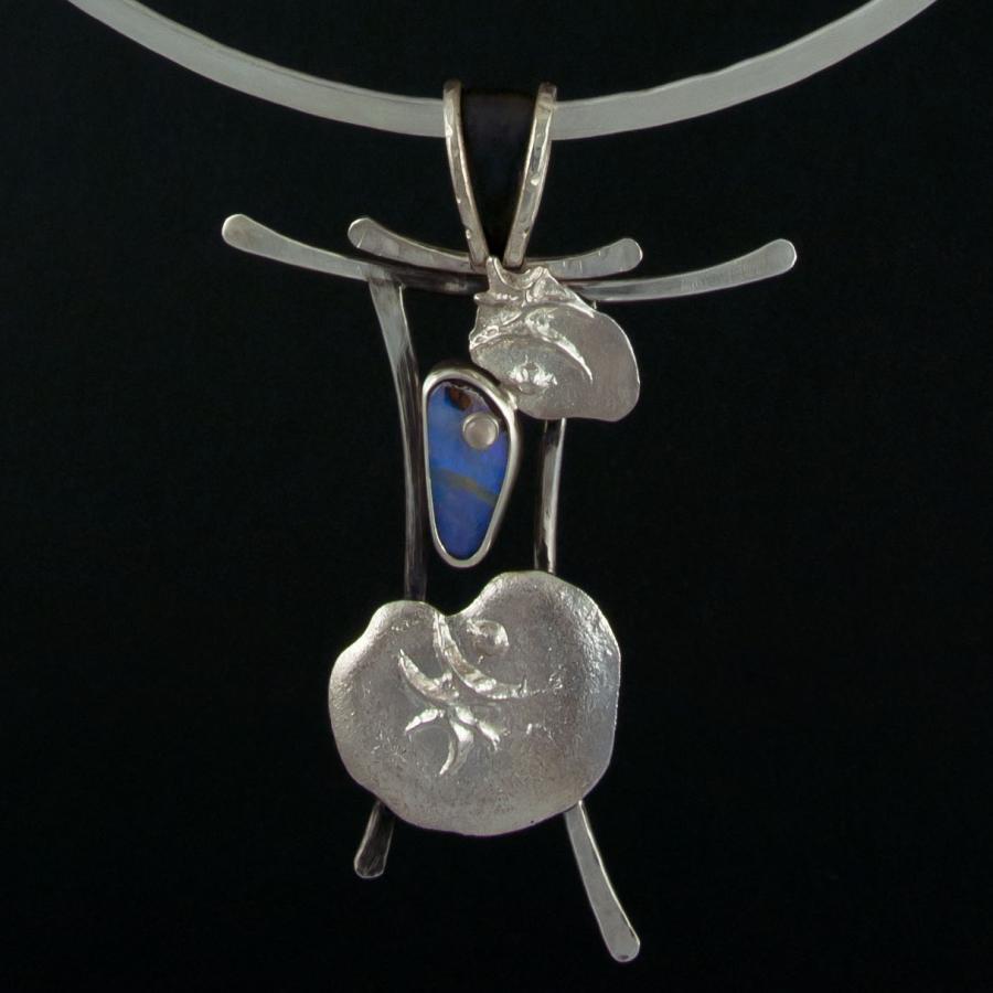Silver necklace with blue stone on black background.