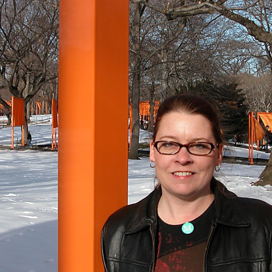 Woman smiles in front of orange art in snowy park.
