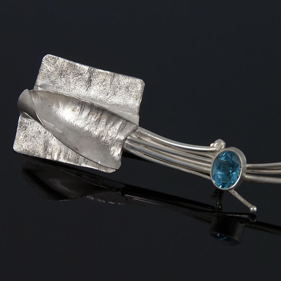 Silver brooch with blue gemstone on black background.