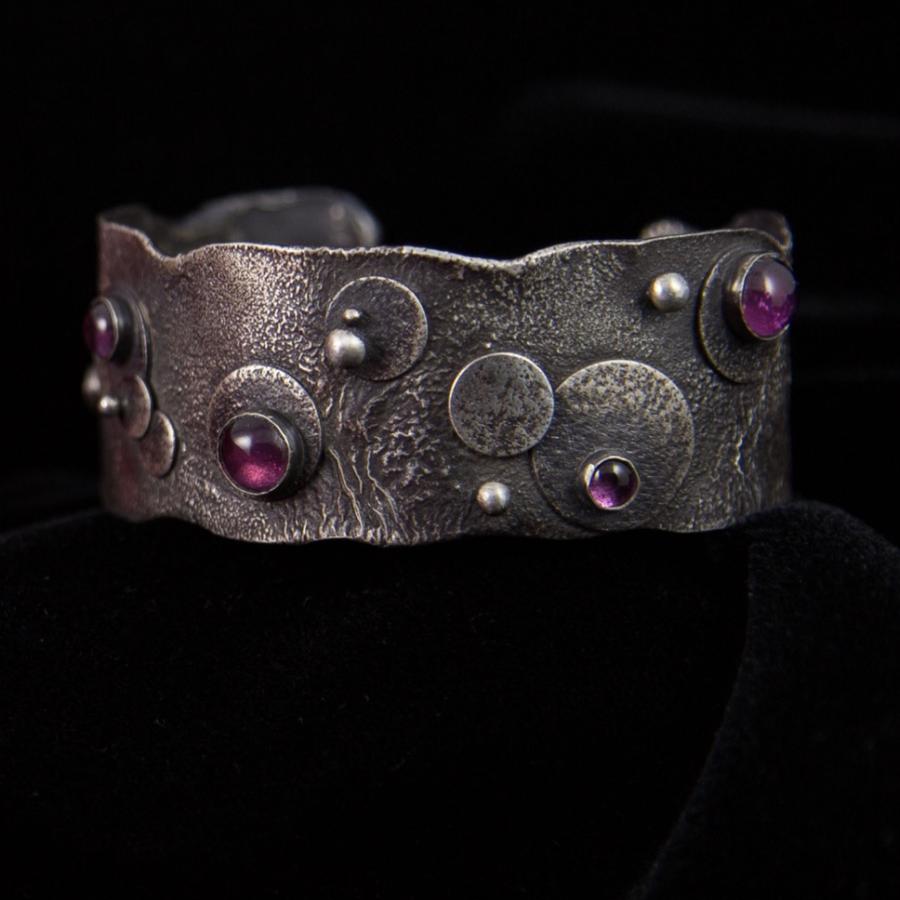 Silver cuff bracelet with red gemstones, studio shot.