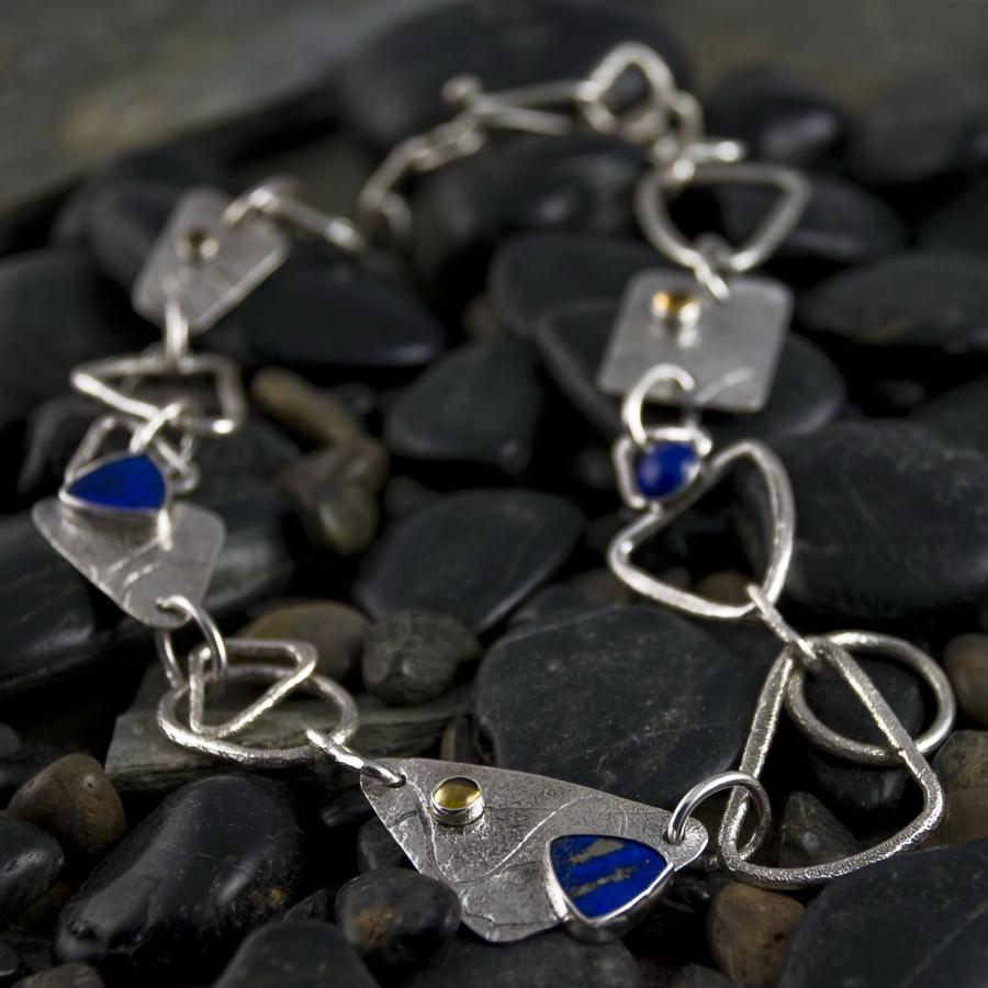 Handmade silver necklace with colorful stones on black rocks.