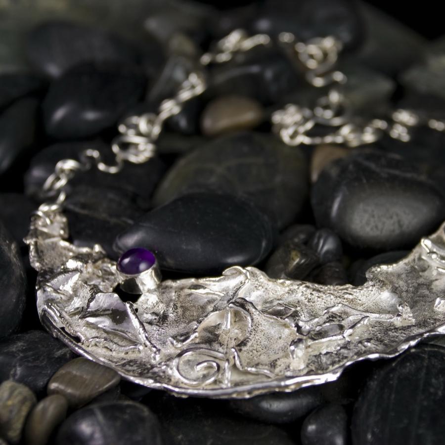Silver necklace with purple stone on black rocks.